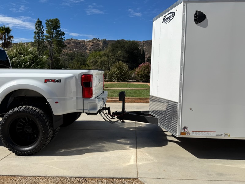 White pickup truck connected to an enclosed trailer, showing the hitch and safety chains
